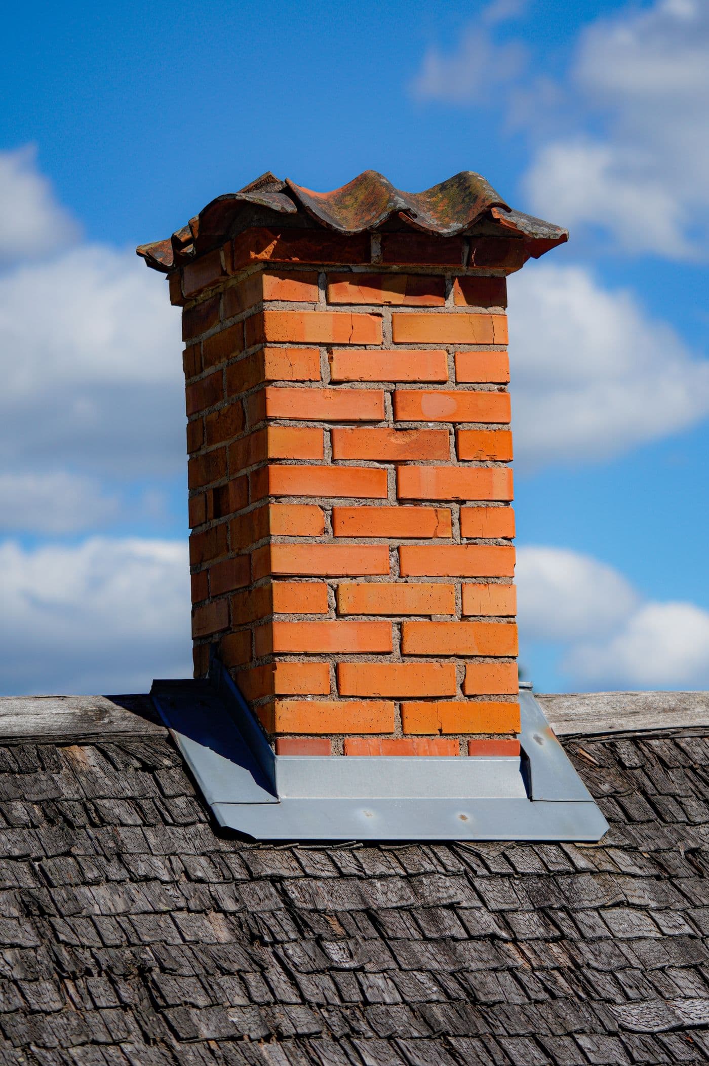 Red brick residential chimney with cap and flashing on a wood-shingle rooftop